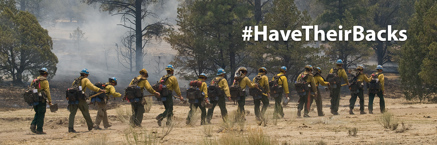 The image shows a wildland fire crew in line. Text above the crew reads, "Have Their Backs."