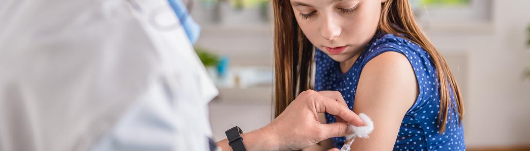 A young girl being vaccinated by a medical staff.