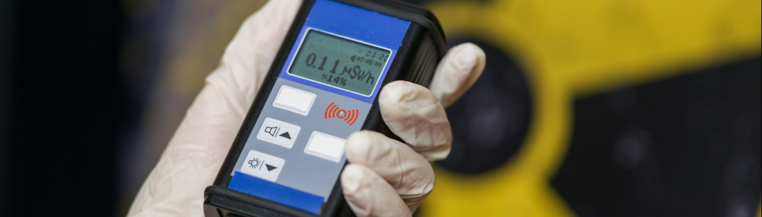 A person holding a device on a gloved hand measuring the radiological level in the space.