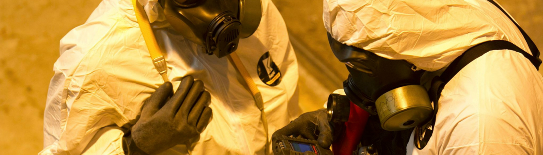 Two men in full hazardous material suits, reading the chemical level in the space.